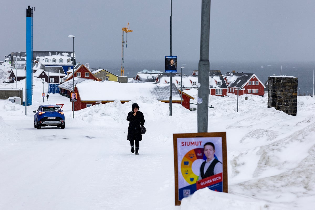 A political poster sits at the side of the road as a woman walks in the snow, in Nuuk, Greenland, on March 8, 2025.