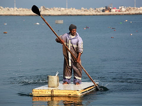 A Palestinian man uses the door of a refrigerator as a makeshift rowing boat to catch fish at the port of Gaza City.