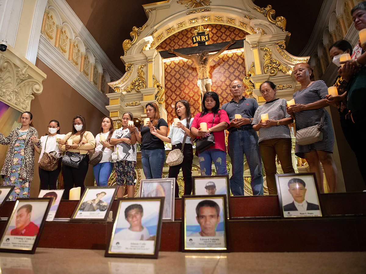 Relatives of victims of former Philippine president Rodrigo Duterte's war on drugs join hands in front of portraits of their deceased loved ones as they hold lit candles during a mass at a church in Manila on March 11, 2025.