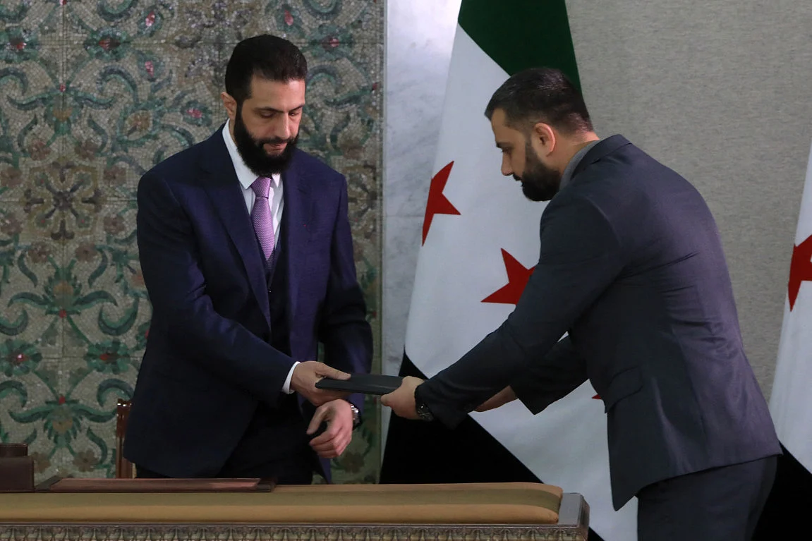 Syria's interim President Ahmad Al Sharaa receives the country's constitutional declaration, which will be enforced throughout a five-year transitional period, before signing it at the presidential palace in Damascus on March 13, 2025.  