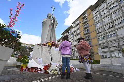 Children pray in front of the statue of John Paul II outside the Gemelli University Hospital where Pope Francis is hospitalised, in Rome on March 16, 2025.