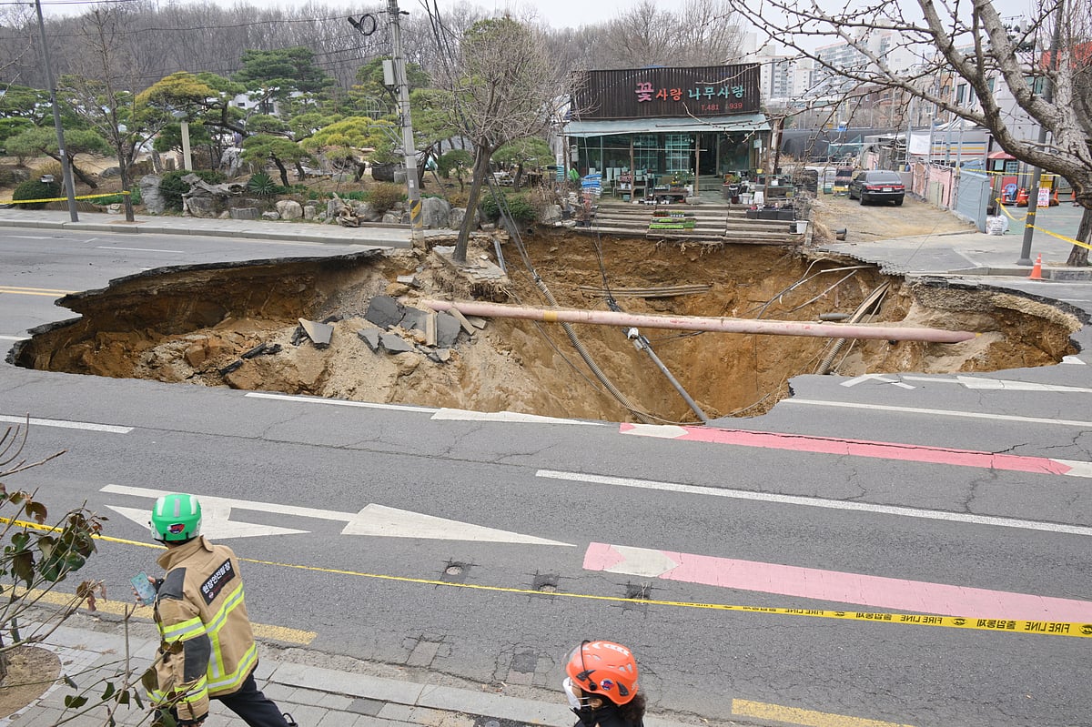 Rescue workers walk past a sinkhole outside a plant shop on a road in Seoul.