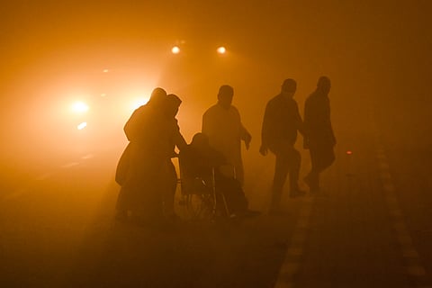A wheelchair-bound person is assisted by others to cross to a traffic island in the middle of a road in low visibility conditions amdist a massive dust storm in Iraq's southern city of Basra on April 14, 2025.