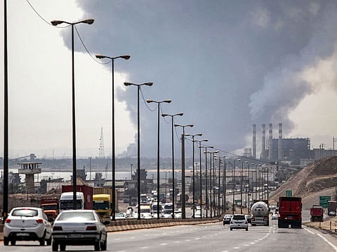 A thick plume of smoke billows as motorists drive their vehicles along a highway near the source of an explosion at the Shahid Rajaee port dock southwest of Bandar Abbas in the Iranian province of Hormozgan.