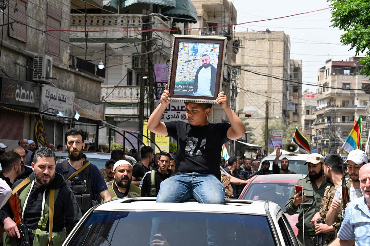 A boy holds a picture of a man as members of Syria's Druze community attend the funeral of seven people killed during overnight clashes with Syrian security forces, in Damascus, on April 30, 2025. 