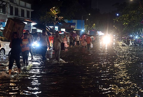 Commuters wade through a waterlogged road as unseasonal rains lash several parts of Mumbai, at Andheri in Mumbai.