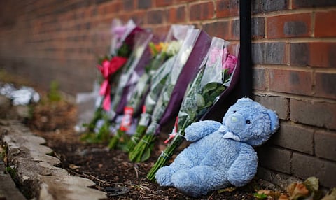 Floral tributes, candles, and a blue teddy bear have been placed near the burnt-out home
