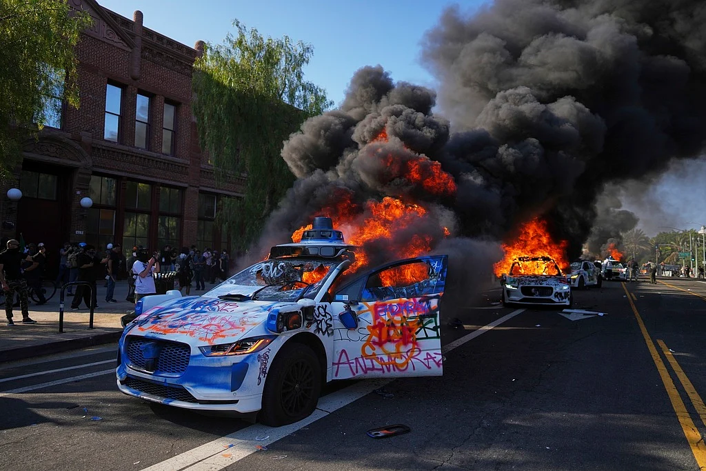 Multiple Waymo taxis burn near the Metropolitan Detention Center of downtown Los Angeles following immigration raid protest.