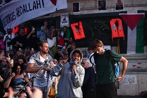 Members of the Gaza-bound aid boat French medical intern Baptiste Andre (R) and activists Reva Viard (L) stand next to French-Palestinian lawyer and member of European Parliament for La France Insoumise (LFI) party Rima Hassan as she speaks during a rally in their support at Place de la Republique in Paris on June 12, 2025, following their deportation after Israel detained her and other activists aboard a Gaza-bound aid boat.