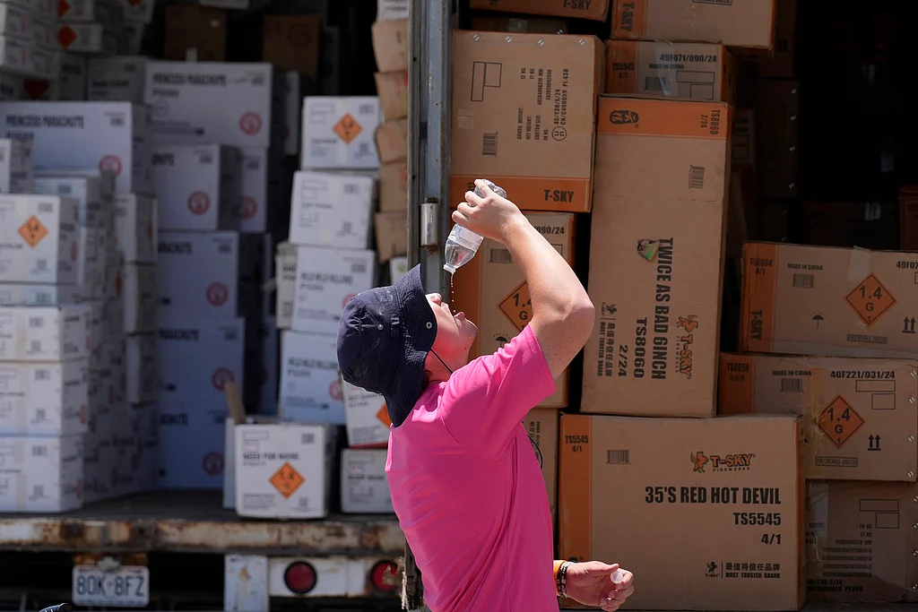 Wyatt Seymore pours the last drops of liquid from a water bottle into his mouth as he takes a break from unloading a stiflingly hot trailer of fireworks outside Powder Monkey Fireworks ahead of the opening of the stand, June 17, 2024, in Weldon Spring, Missouri.  