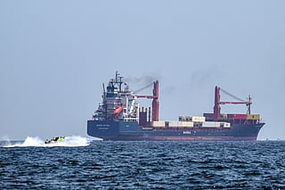 A boat approaches the container ship Marsa Victory while crusing in the waters of the Strait of Hormuz off the coast of Khasab in Oman’s northern Musandam peninsula on June 25, 2025.