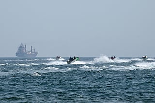 Small boats loaded with merchandise sail past the St Kitt's and Nevis-flagged container ship Marsa Victory while crusing in the waters of the Strait of Hormuz off the coast of Khasab in Oman’s northern Musandam peninsula on June 25, 2025.