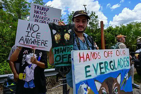 Demonstrators hold signs as they protest U.S. President Donald Trump's visit to a migrant detention centre, dubbed "Alligator Alcatraz." 
