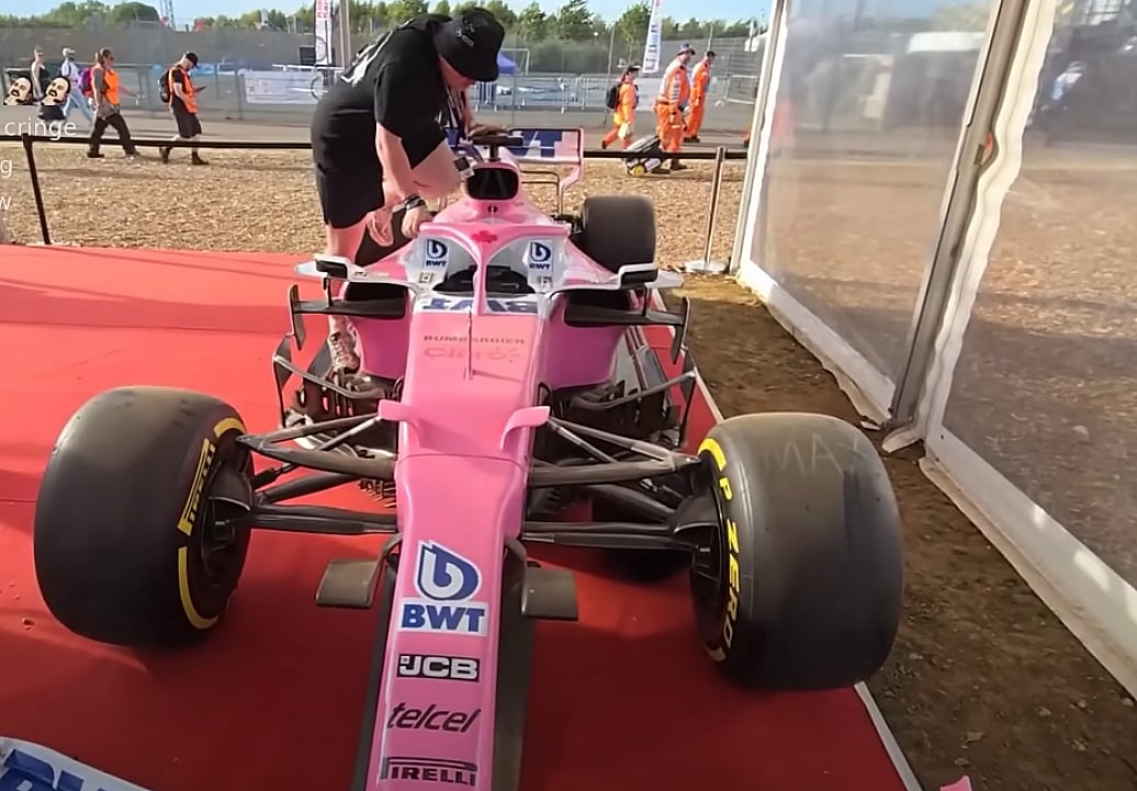 A YouTuber attempting to squeeze into the cockpit of a 2019 Racing Point F1 car, part of a public display at Silverstone.