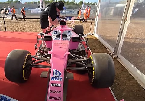 A YouTuber attempting to squeeze into the cockpit of a 2019 Racing Point F1 car, part of a public display at Silverstone.