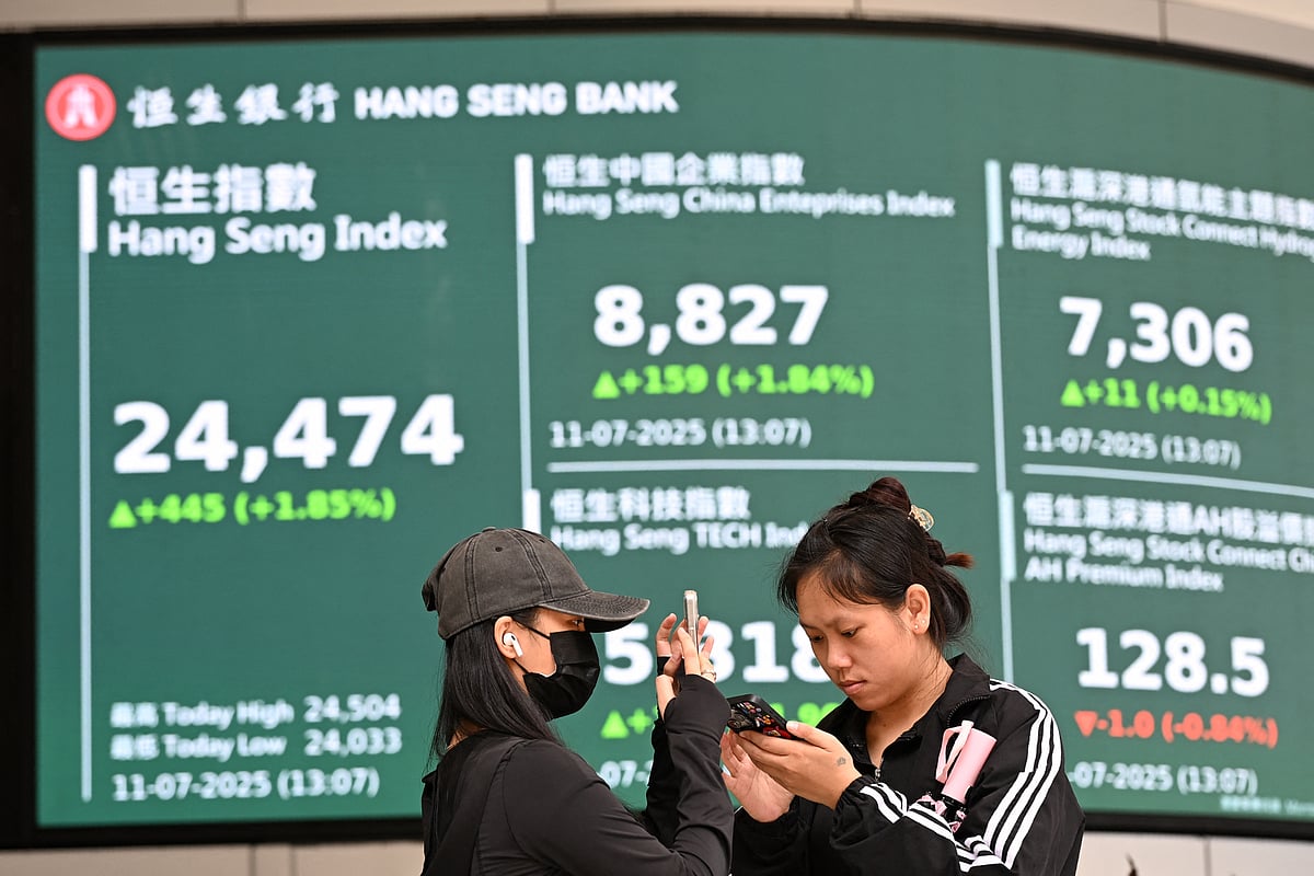 Woman check their phones in front of an electronic sign board showing the the Hang Seng Index in Hong Kong. File photo taken on July 11, 2025.