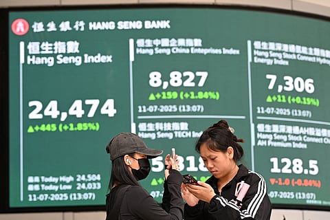 Woman check their phones in front of an electronic sign board showing the the Hang Seng Index in Hong Kong. File photo taken on July 11, 2025.