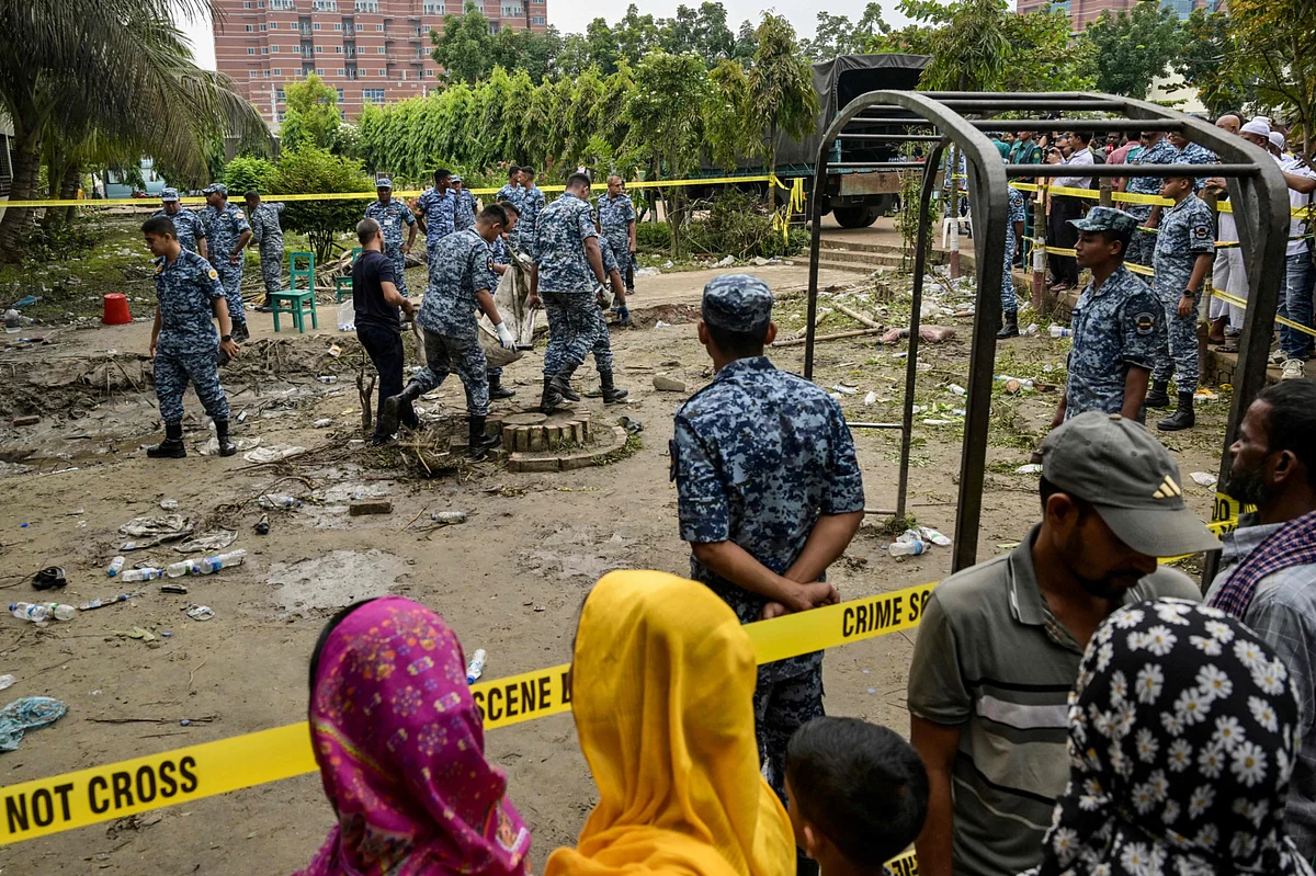 Onlookers gather as Bangladesh Air Force personnel recover debris while inspecting the crash site, a day after a training jet crashed into a school in Dhaka on July 22, 2025. 