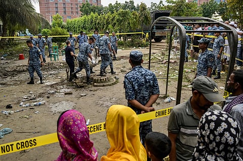 Onlookers gather as Bangladesh Air Force personnel recover debris while inspecting the crash site, a day after a training jet crashed into a school in Dhaka on July 22, 2025. 
