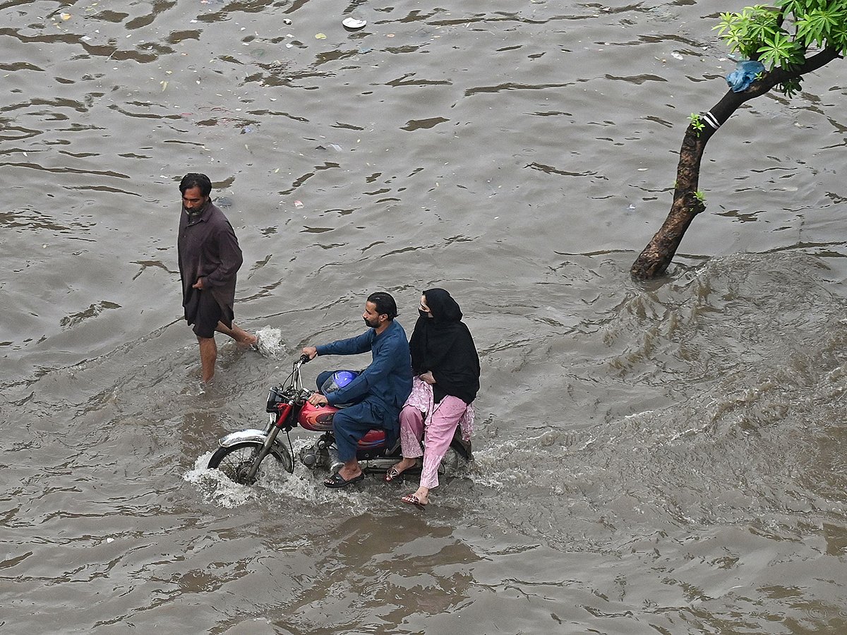 Commuters wade through a flooded street after heavy rainfall in Lahore on July 23, 2025.  