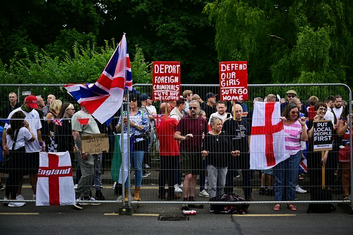 Anti-immigrant protestors hold placards reading "Deport foreign criminals, SUTR (Stand Up To Racism) go home" and "Defend our girls, SUTR (Stand Up To Racism) go home" as they demonstrate behind fences outside The Bell Hotel believed to be housing asylum seekers, in Epping, northest of London, on July 27, 2025, after police charged an asylum-seeker with sexual offences earlier this month.