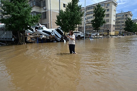 A woman makes a phone call while wading in a flooded street in Miyun district northern Beijing on July 29, 2025, following heavy rains.