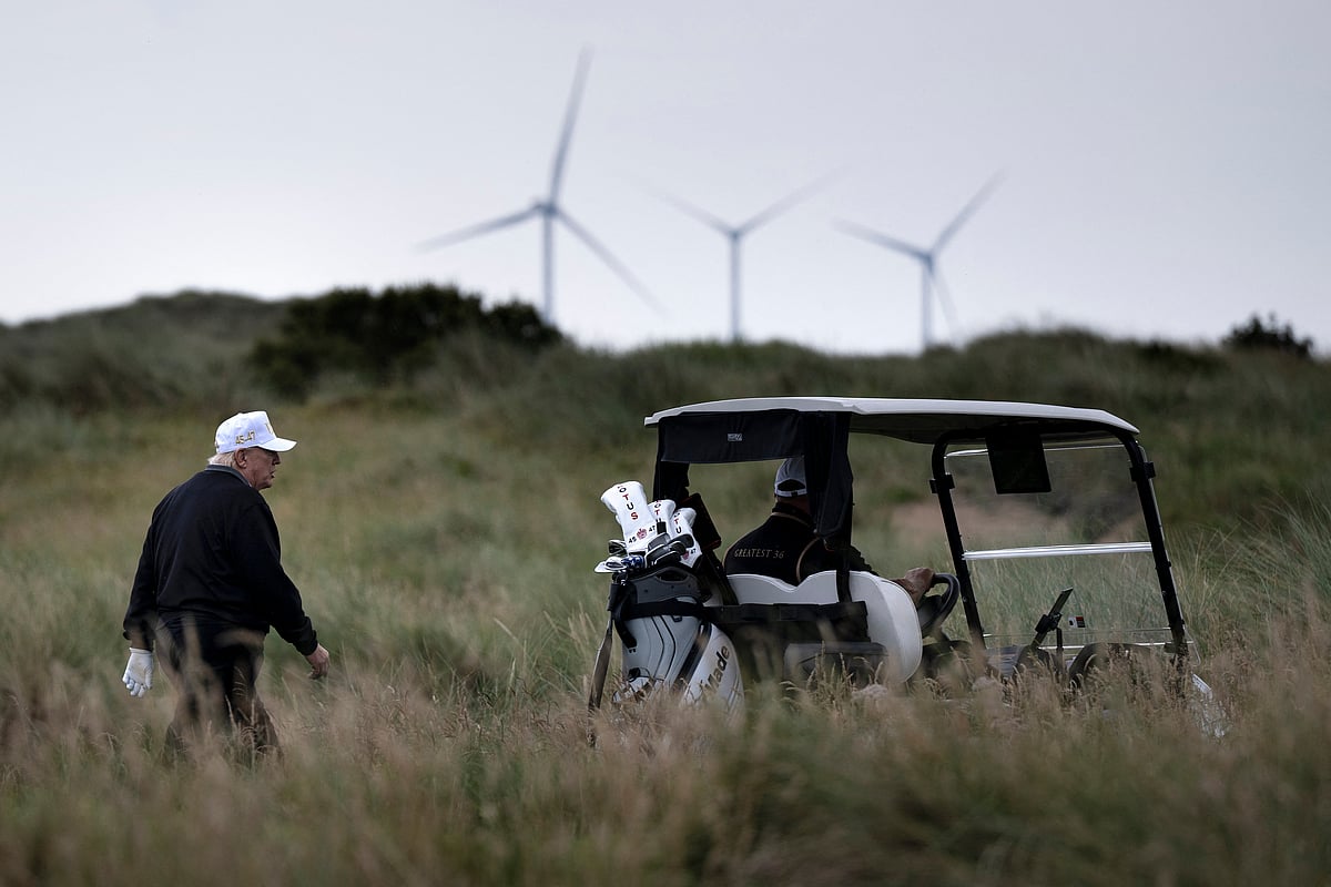 US President Donald Trump (L), backdropped by Turbines at the European Offshore Wind Deployment Centre, also known as the Aberdeen Bay Wind Farm, walks on the first fairway after playing off the first tee to officially open the Trump International Golf Links course in Balmedie, Aberdeenshire, north east Scotland on July 29, 2025.
