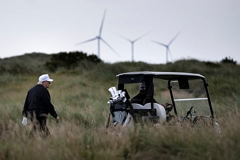 US President Donald Trump (L), backdropped by Turbines at the European Offshore Wind Deployment Centre, also known as the Aberdeen Bay Wind Farm, walks on the first fairway after playing off the first tee to officially open the Trump International Golf Links course in Balmedie, Aberdeenshire, north east Scotland on July 29, 2025.