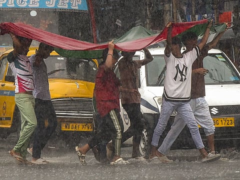 People cover themselves to get protection from heavy rain, in Kolkata on Tuesday.