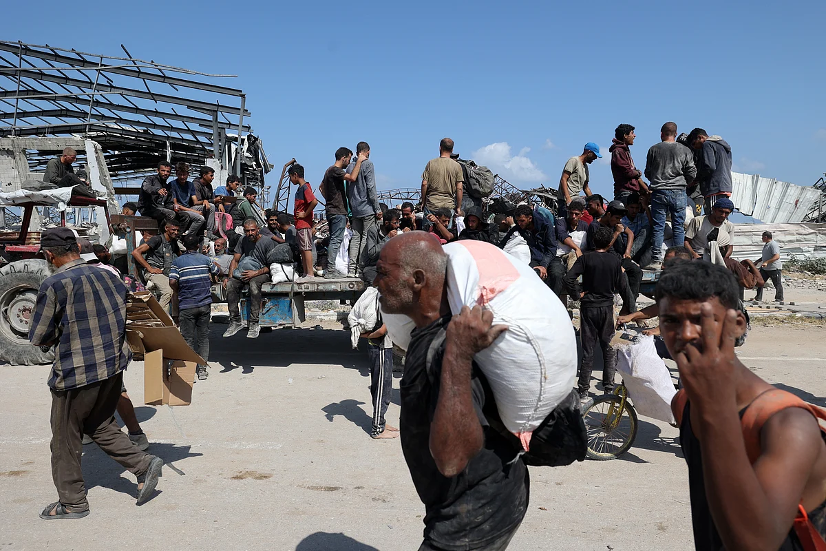 Palestinians transport bags as they return from a food distribution point run by the US and Israeli-backed Gaza Humanitarian Foundation (GHF) group, near the Netsarim corridor in the central Gaza Strip on August 3, 2025.