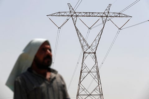 An Iraqi stands under an electricity transmission tower south of Hilla city on August 10, 2025, amidst rising temperatures, chronic water shortages and power cuts.
