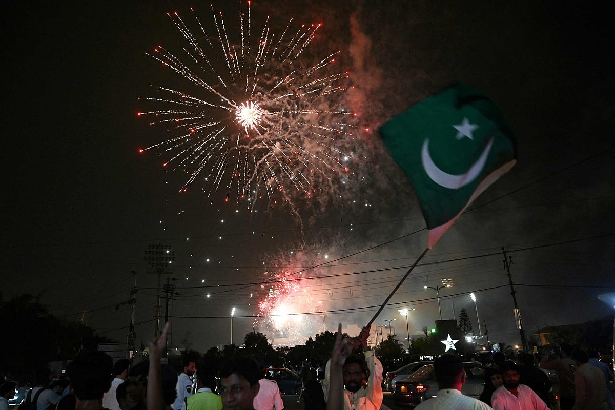 A man waves a flag of Pakistan as people watch a firework displayed in front of the National Stadium during Pakistan's 78th anniversary of Independence Day celebrations in Karachi on August 14, 2025. 