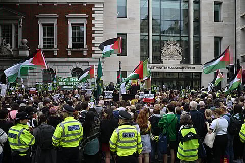 Metropolitan Police officers stand on duty as supporters of the band Kneecap, and its singer Liam O'Hanna who performs under the stage name Mo Chara, fly Palestinian flags outside Westminster Magistrates' Courts in London on August 20, 2025, as O'Hanna arrived to appear charged with a terror offence.