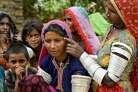 A villager in traditional attire pointing to an indigenous tattoo inked on Reshma's  face at the Ponjo Kolhi village, about 30 km from Umerkot, a Hindu-majority district in Pakistan. In rural Sindh province, Pakistan, the centuries-old tradition of tattooing young Hindu girls’ faces, hands, and arms is slowly fading. 