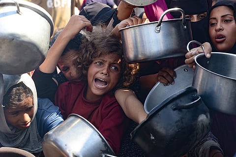 Palestinian women and children hold out their empty pots in front of a charity kitchen in Khan Yunis in the southern Gaza Strip.
