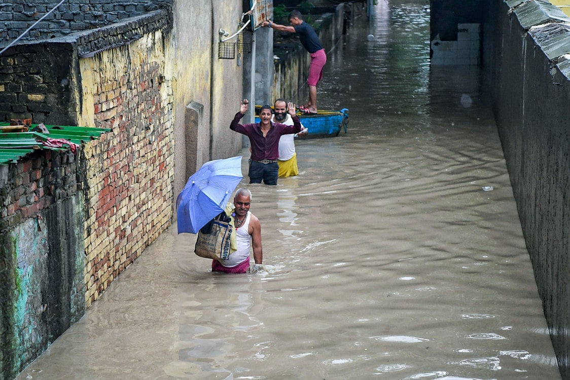 People walk through a waterlogged area as the river Yamuna crosses the danger mark following incessant rainfall, at Yamuna Bazar in New Delhi on Tuesday.  