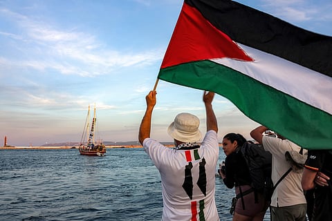 A man waves a Palestinian flags to other activists and human rights defenders riding aboard a vessel departing from Tunisia's northern port of Bizerte on September 14, 2025 to join the last boats taking part in the Global Sumud Flotilla, bound for the Gaza Strip to break Israel's blockade on the Palestinian territory.