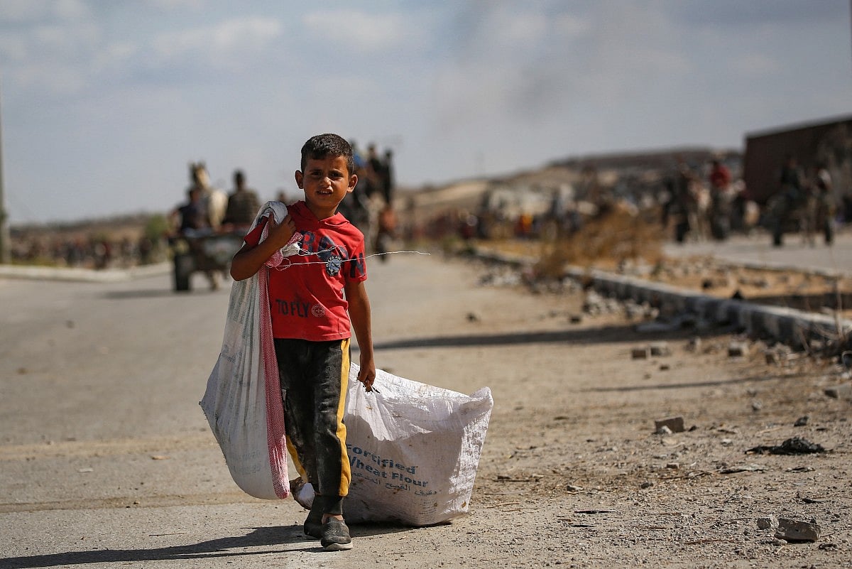 A Palestinian boy carries a bag and drags another behind him as he returns from a food distribution point run by the US and Israeli-backed Gaza Humanitarian Foundation (GHF) group, near the Netsarim corridor in the central Gaza Strip on October 5, 2025.