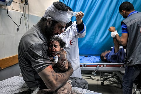 An injured man holds another injured child, both survivors of Israeli bombardment, while a nurse bandages his head at a trauma ward at Nasser hospital in Khan Yunis in the southern Gaza Strip on October 24, 2023. 