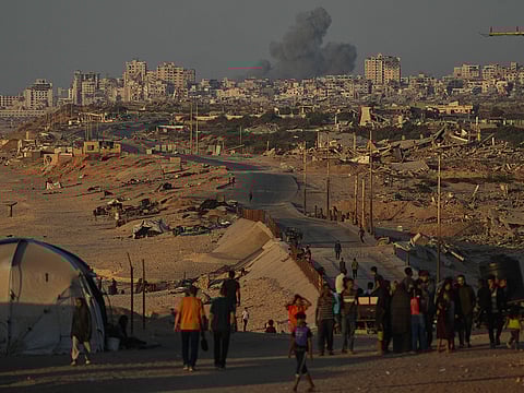 Displaced Palestinians walk along the coastal road, backdropped by smoke rising into the sky in Gaza City on Wednesday October 8.