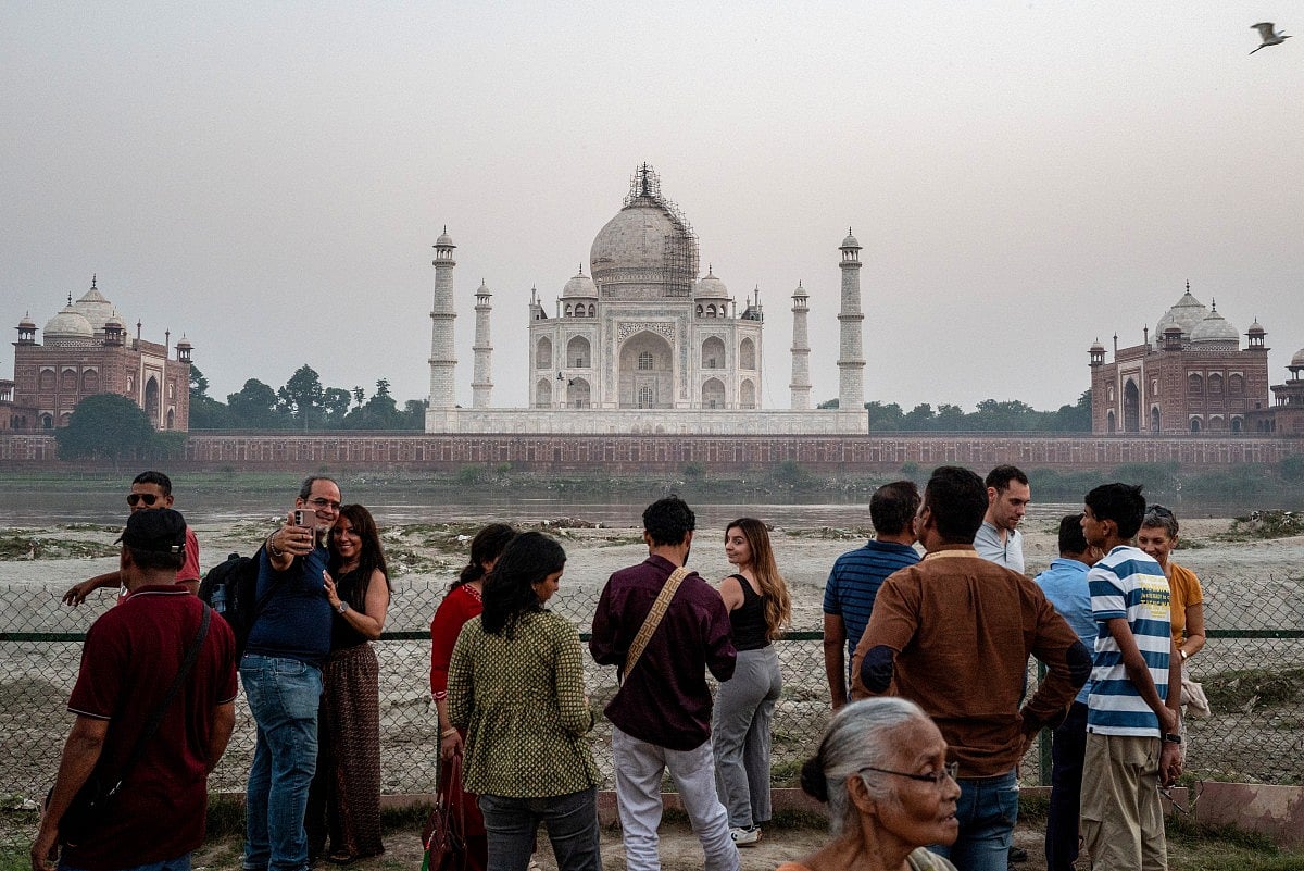 Tourists click photographs with the backdrop of the Taj Mahal in Agra on October 17, 2025.