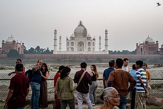 Tourists click photographs with the backdrop of the Taj Mahal in Agra on October 17, 2025.