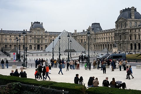 Tourists and visitors walk in front of the Louvre Museum next to French police officers (C) after the museum was closed following a robbery, in Paris on October 19, 2025.