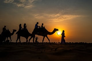 Tourists ride camels at a desert resort in Dubai at sunset on October 19, 2025.