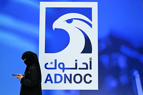 A guest looks at her phone as she stands at the booth of the Abu Dhabi National Oil Company (ADNOC), during the Abu Dhabi International Petroleum Exhibition & Conference (ADIPEC) in Abu Dhabi on November 3, 2025.