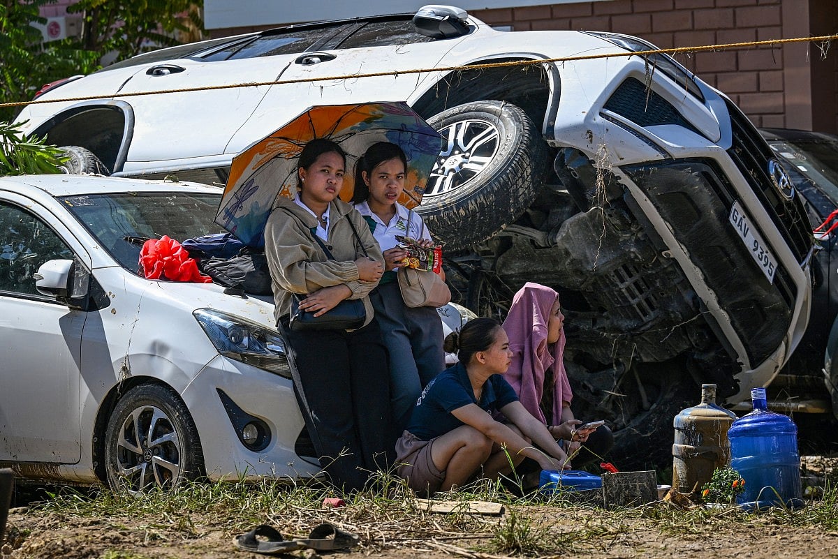 People rest beside cars, swept one on top of another by floodwaters caused by typhoon Kalmaegi, in Liloan in the province of Cebu on November 6, 2025.