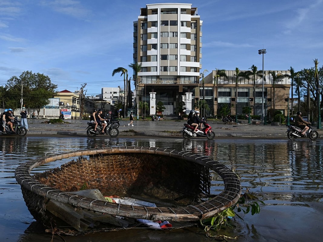 Motorists ride past pools of water and a coracle boat swept inland by typhoon Kalmaegi in Quy Nhon in Gia Lai province, central Vietnam on November 7, 2025.
