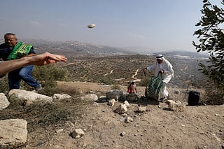 A Palestinian man throws a stone towards Israeli soldiers (unseen) as a Palestinian man run for cover from tear gas, during a protest against the confiscation of land by Israeli settlers near the village Kfar Qaddum, east of the Israeli occupied West Bank city of Nablus, on November 7, 2025.
