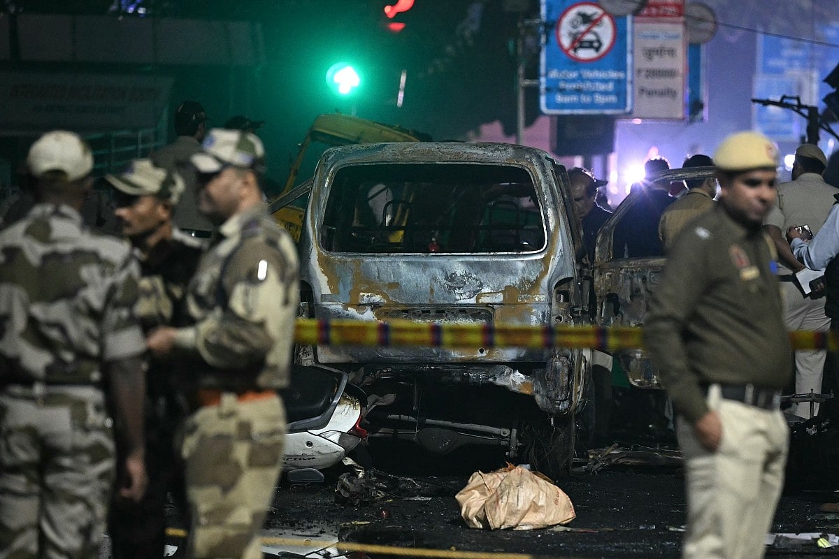 Security personnel stand beside a charred vehicle at the blast site after an explosion near the Red Fort in the old quarters of Delhi on November 10, 2025.