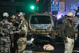 Security personnel stand beside a charred vehicle at the blast site after an explosion near the Red Fort in the old quarters of Delhi on November 10, 2025.